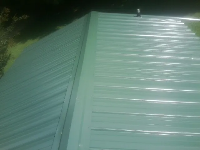 New green metal panels meeting at the ridge of a roof — Flat Roof Repair work by our crew in Marion